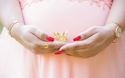 Midsection of pregnant woman holding small crown