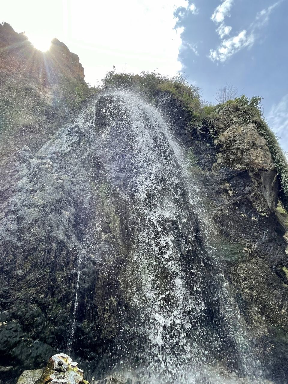 waterfall, nature, sky, water feature, rock, water, mountain, cliff, beauty in nature, scenics - nature, day, motion, sunlight, environment, no people, splashing, terrain, cloud, land, outdoors, landscape, plant, non-urban scene, tree, low angle view, geology, lens flare, ridge, mountain range