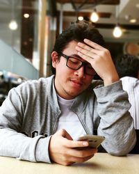 Young man using mobile phone while sitting on chair and desk