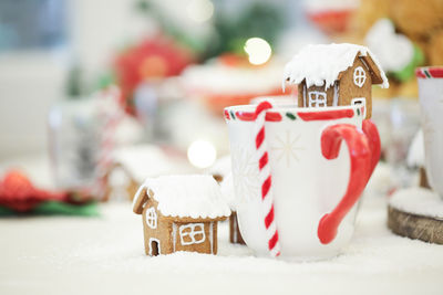 Close-up of gingerbread house and white mugs decorated on table during christmas