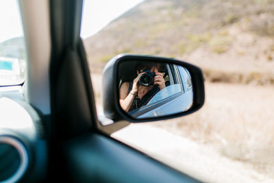 Reflection of woman photographing through side-view mirror of car