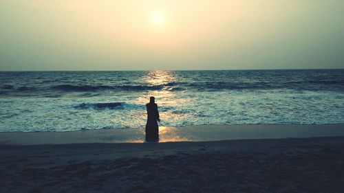 Silhouette people standing on beach against sky during sunset