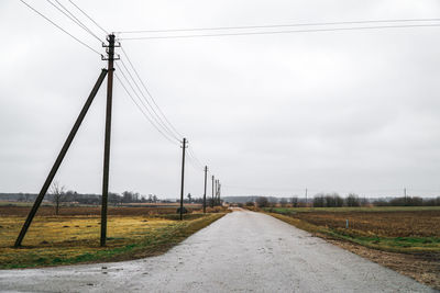 Road by electricity pylon against sky