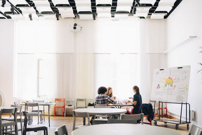 Multi-ethnic team of technicians working at table by whiteboard in creative office