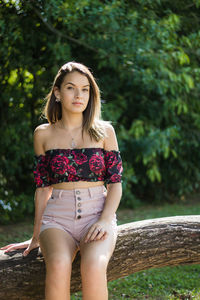Portrait of teenage girl sitting on tree trunk against plants in park