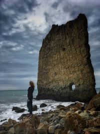 Man standing on rock by sea against sky