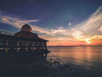 Built structure on beach against sky during sunset