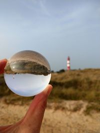 Close-up of hand holding lighthouse against sky