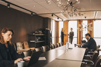 Male and female lawyers working at conference table while colleagues discussing in background