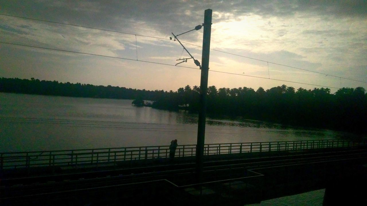 SILHOUETTE ELECTRICITY PYLON BY RIVER AGAINST SKY DURING SUNSET