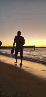 Silhouette man standing on beach against sky during sunset