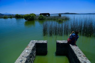 Rear view of woman by lake against sky