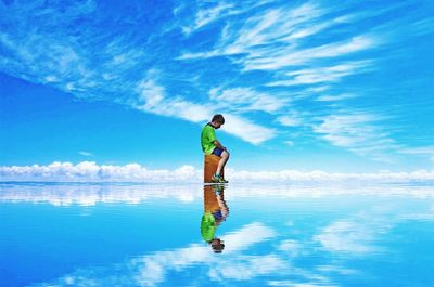 Digital composite image of boy sitting on stool in sea against sky