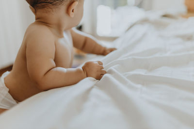 Midsection of shirtless baby lying on bed