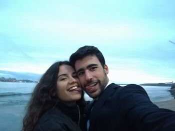 Portrait of smiling young couple on beach against sky