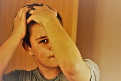 Portrait of young man with hand in hair by wall at home