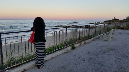 Rear view of woman standing on beach against clear sky