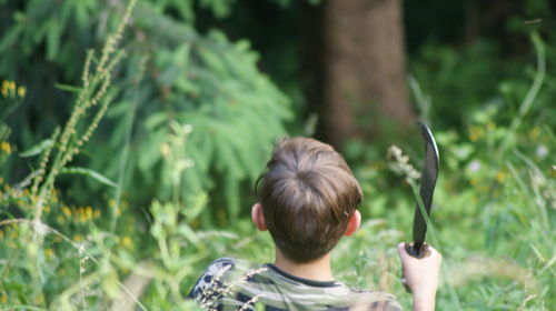 Rear view of boy holding tool in forest