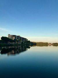 Scenic view of lake by buildings against clear blue sky