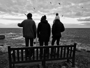 Rear view of friends standing on bench against sea at beach