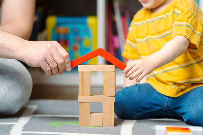 Father and son are holding a roof for a wooden house in their hands. 