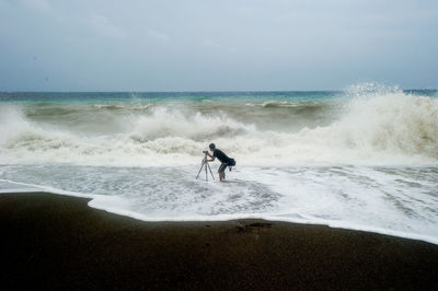 Man photographing while standing on shore at beach against sky