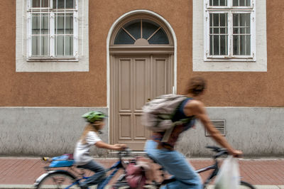 Blurred motion of mother and daughter riding bicycles against building