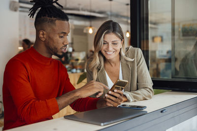 Businessman sharing smart phone with colleague at cafe