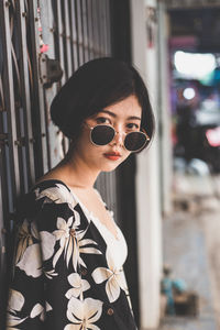 Portrait of young woman wearing sunglasses while standing against gate