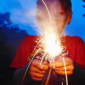 Close-up of hand holding sparkler against sky