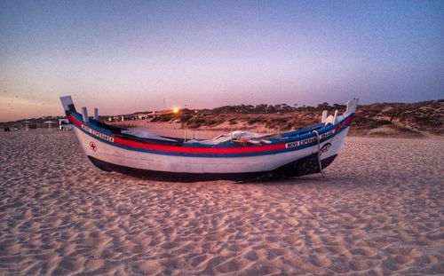 Boats moored on beach against clear sky during sunset