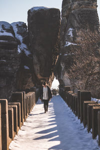 Woman walking on frozen footbridge against rock formations