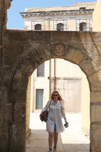 Mature woman walking below arch at old ruins