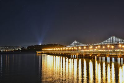 Illuminated bridge over river against sky at night