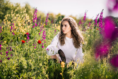 Beautiful young woman with pink wild flowers in sunlight during summer