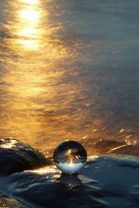 Close-up of crystal ball in sea against sunset sky