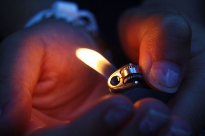 Close-up of cropped hands lighting cigarette lighter at night