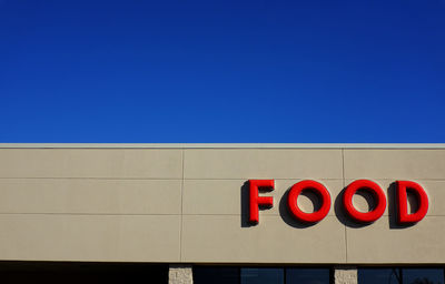 Low angle view of food text on building against clear blue sky on sunny day