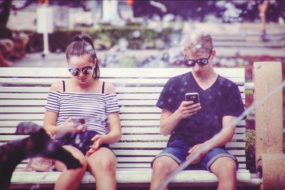 Friends using smart phone while sitting on bench at park
