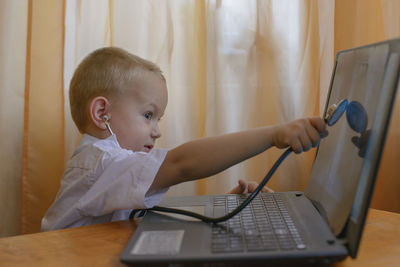 Boy wearing stethoscope while using laptop at table