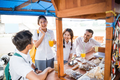 Portrait of smiling friends using mobile phone while sitting on table