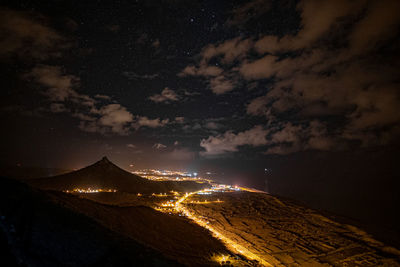 Aerial view of illuminated city against cloudy sky at night