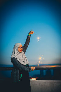 Woman with burning sparklers against blue sky at dusk