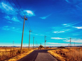 Road by electricity pylon against blue sky