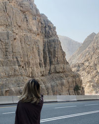 Rear view of woman standing on road against rocky mountains