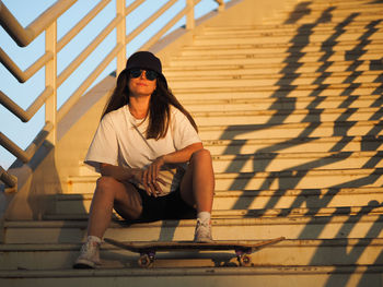 Stylish european young woman skater sitting on concrete staircase.