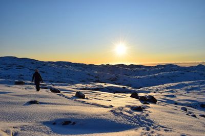 Full length of hiker walking on snow against sky during sunset