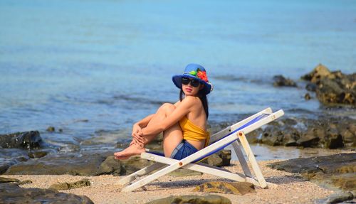 Full length of shirtless man sitting at beach