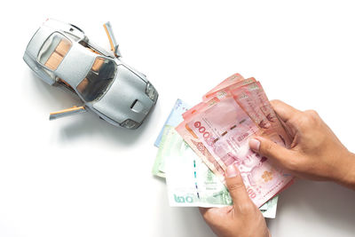 Cropped hand holding paper currency with toy car against white background