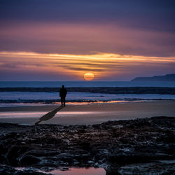 Silhouette man standing on sea shore at beach during sunset